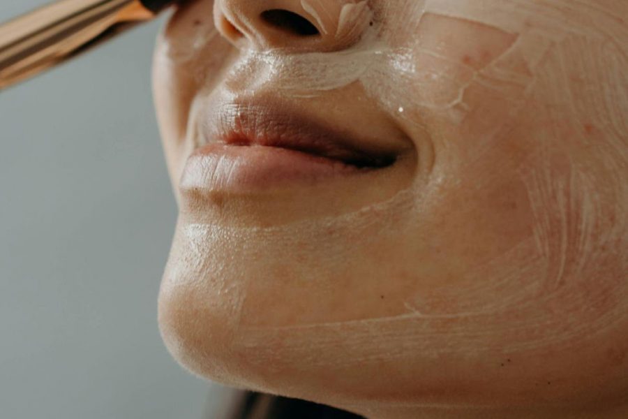 An Asian woman applying a clay mask using a brush onto her clean skin
